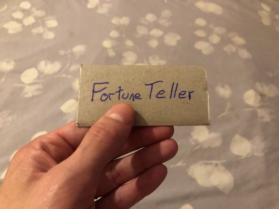 A small cardstock envelope, held over a bed, with Fortune Teller written on the front.