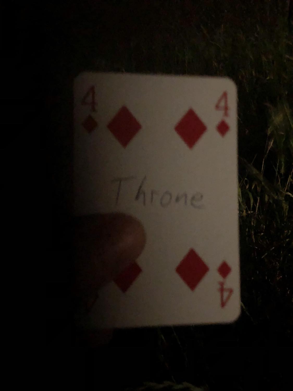 The four of diamonds with the word Throne written on it, held in the barely lit dark.