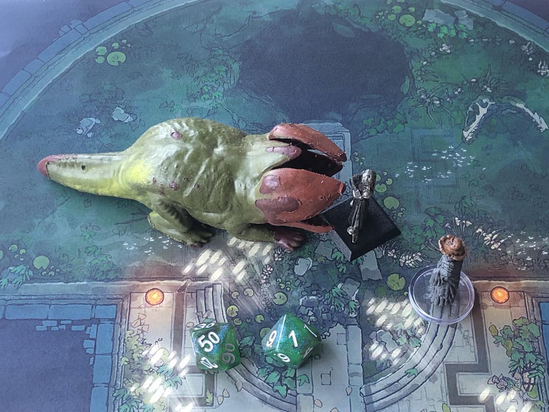 The battle map from above, with the monk fully attacking the creature, and the sorcerer rolling a pair of d10 dice to determine the wild magic surge.